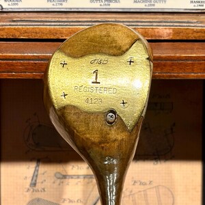 May include: Antique wooden golf club with a brass face. The club head is marked with "H&B", the number "1", and the word "REGISTERED" along with the number "4123". The club has a dark wood finish.