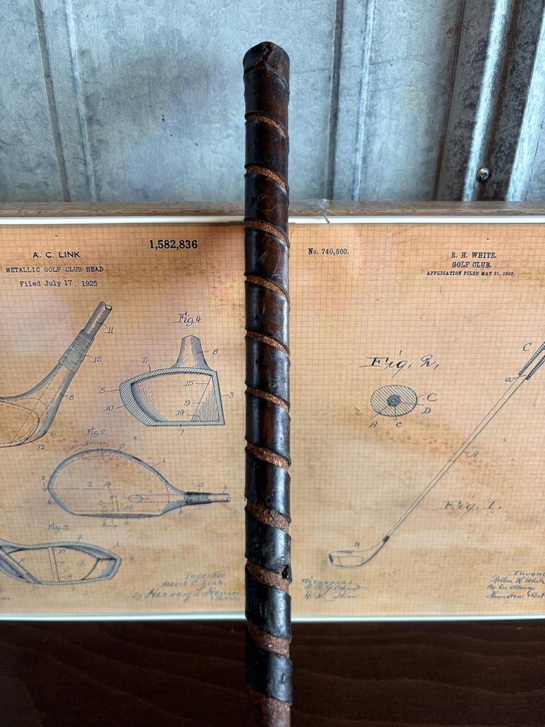 Puede incluir: Un primer plano de una empu&ntilde;adura de palo de golf de cuero marr&oacute;n con un dise&ntilde;o trenzado marr&oacute;n y negro. La empu&ntilde;adura est&aacute; envuelta alrededor de un eje de madera. La imagen est&aacute; enmarcada e incluye un dibujo de patente para una cabeza de palo de golf.