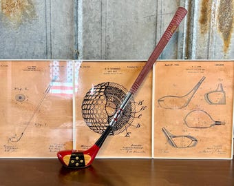May include: Three framed vintage patent drawings of golf clubs and golf balls. The drawings are in black and white on a tan background. A miniature red and black golf club is in the foreground.