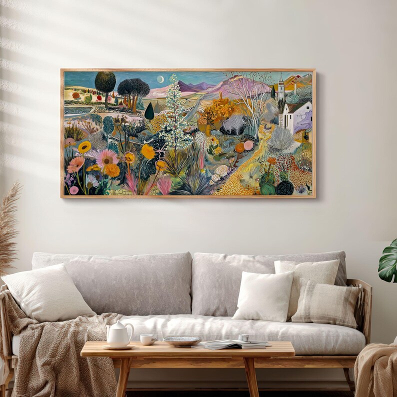May include: A framed landscape painting with a wooden frame. The artwork depicts a colorful scene with flowers, trees, and a path leading to a village. The color palette includes blues, greens, yellows, and oranges. The painting is displayed above a sofa.