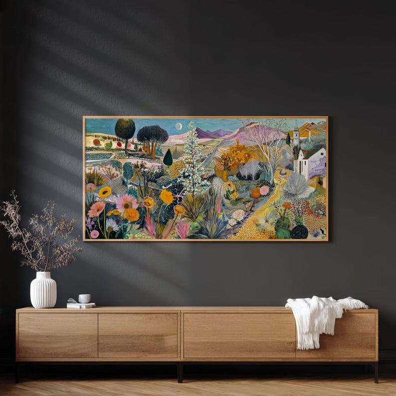 May include: A framed landscape painting depicts a vibrant garden scene with colorful flowers, trees, and a distant mountain range. The artwork features a variety of hues, including pink, yellow, green, and blue, creating a lively and detailed composition. The painting is displayed above a wooden cabinet.