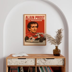 May include: A framed poster of Alain Prost, with the text "ALAIN PROST LE PROFESSEUR" in red and white. The poster includes a portrait of Prost and an image of his race car, with "Marlboro" and "Shell" branding.