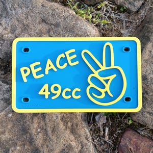 May include: A blue and yellow license plate with the word "PEACE" and a peace sign. The plate also has the text "49cc" in yellow.
