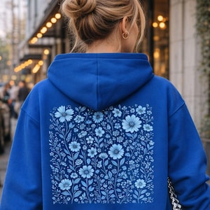 Könnte beinhalten: Ein königsblauer Hoodie mit einem Blumendesign auf dem Rücken. Das Blumenmuster zeigt verschiedene Blautöne von Blumen und Blättern. Der Hoodie hat eine Kapuze und einen Kordelzug.