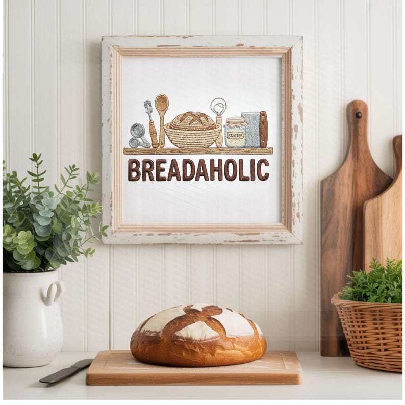 May include: A framed print with the word "BREADAHOLIC" and illustrations of baking tools. A loaf of bread sits on a wooden cutting board in front of the print. The print is in a white distressed frame.