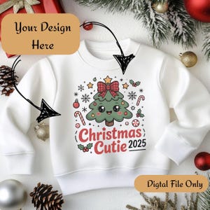 Puede incluir: Sudadera blanca con un diseño de árbol de Navidad, lazo rojo, estrellas y bastones de caramelo. El texto dice "Christmas Cutie 2025". La sudadera tiene cuello redondo y mangas largas. Las palabras "Your Design Here" y "Digital File Only" también son visibles.