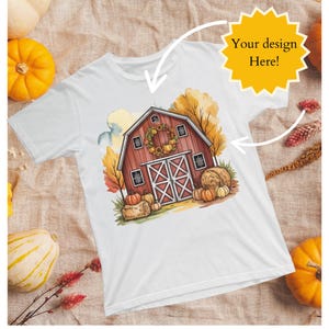 May include: White t-shirt featuring a watercolor illustration of a red barn with a wreath, pumpkins, and hay bales. The text "Your design Here!" is in a yellow starburst. The shirt has a crew neck and short sleeves.