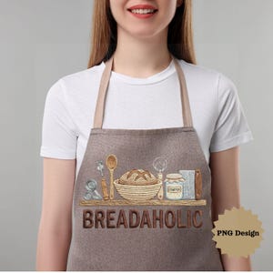 May include: A brown apron with a tan neck strap and the word "BREADAHOLIC" embroidered on the front. The apron features an embroidered shelf with bread-making tools and a loaf of bread. A small graphic says "PNG Design".