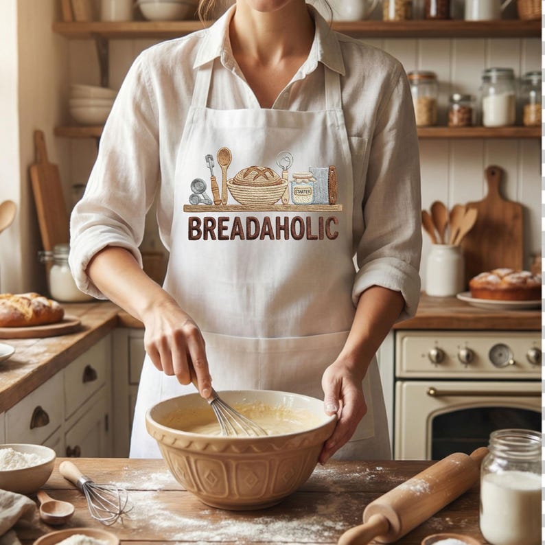 May include: A person wearing a white apron with the text "BREADAHOLIC" and a bread-themed graphic. The person is whisking ingredients in a brown bowl. Baking tools and ingredients are on the wooden counter.