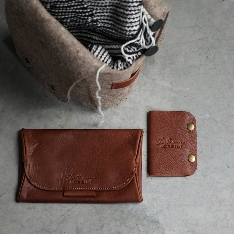 May include: Two brown leather wallets with the text "Le Rouge Habilleur" embossed on them. The wallets are on a gray surface.