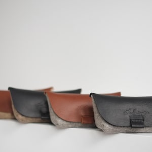 May include: Four felt eyeglass cases in different colors. The cases are lined with a soft gray felt and have a leather flap with a snap closure. The case on the right has the text "La Grange" embossed on the flap.