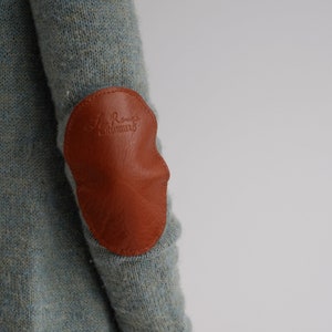 Peut inclure: Un pull bleu clair avec un coude en cuir marron. Le patch porte le texte "Le Rouge" et "L'HABILLEUR" en relief.