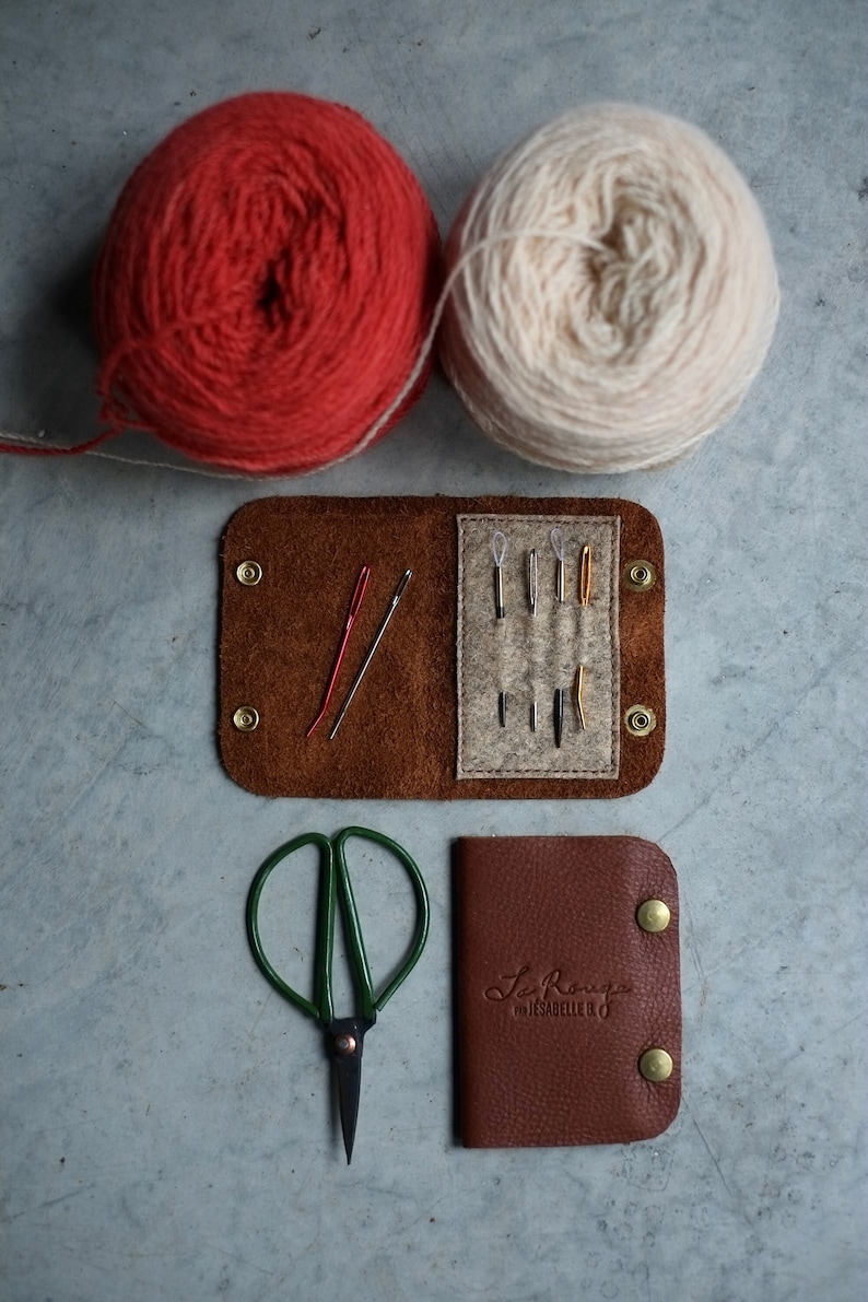 May include: A brown leather sewing kit with a flap that opens to reveal a felt interior with needles and thread. The kit also includes a pair of small green scissors and a separate brown leather pouch with the text "Le Rouge" and "Made by Isabelle B."