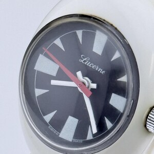 Puede incluir: Un reloj de pulsera Lucerne blanco con esfera negra y agujas blancas y rojas. La esfera del reloj tiene marcadores de hora triangulares blancos y las palabras "Lucerne", "Swiss" y "Made".