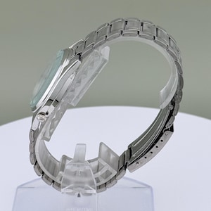 Pu&ograve; includere: Un orologio da polso argentato con quadrante azzurro e cinturino in acciaio inossidabile. L'orologio &egrave; esposto su un supporto di plastica trasparente, che ne mette in risalto il design elegante e la finitura metallica. Il cinturino &egrave; composto da maglie.