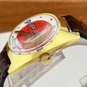 May include: A vintage wristwatch with a gold-toned case and a brown leather strap. The watch face features a red and white design with the text "Spin" and blue star accents. The watch has a gold crown.