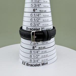 May include: A black leather bracelet with white stitching and a silver buckle is displayed on a white and black bracelet sizing cone. The cone measures from 5 inches (12.7 cm) to 8 3/4 inches (22.2 cm). The text "EZ Bracelet Mini" is visible.