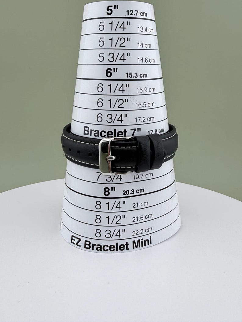 May include: A black leather bracelet with white stitching and a silver buckle is displayed on a white and black bracelet sizing cone. The cone measures from 5 inches (12.7 cm) to 8 3/4 inches (22.2 cm). The text "EZ Bracelet Mini" is visible.