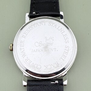 May include: Close-up of the back of a silver-toned watch with a black leather band. The watch face reads "WATER RESISTANT STAINLESS STEEL BACK COVER" and "Swanvie JAPAN OVT."