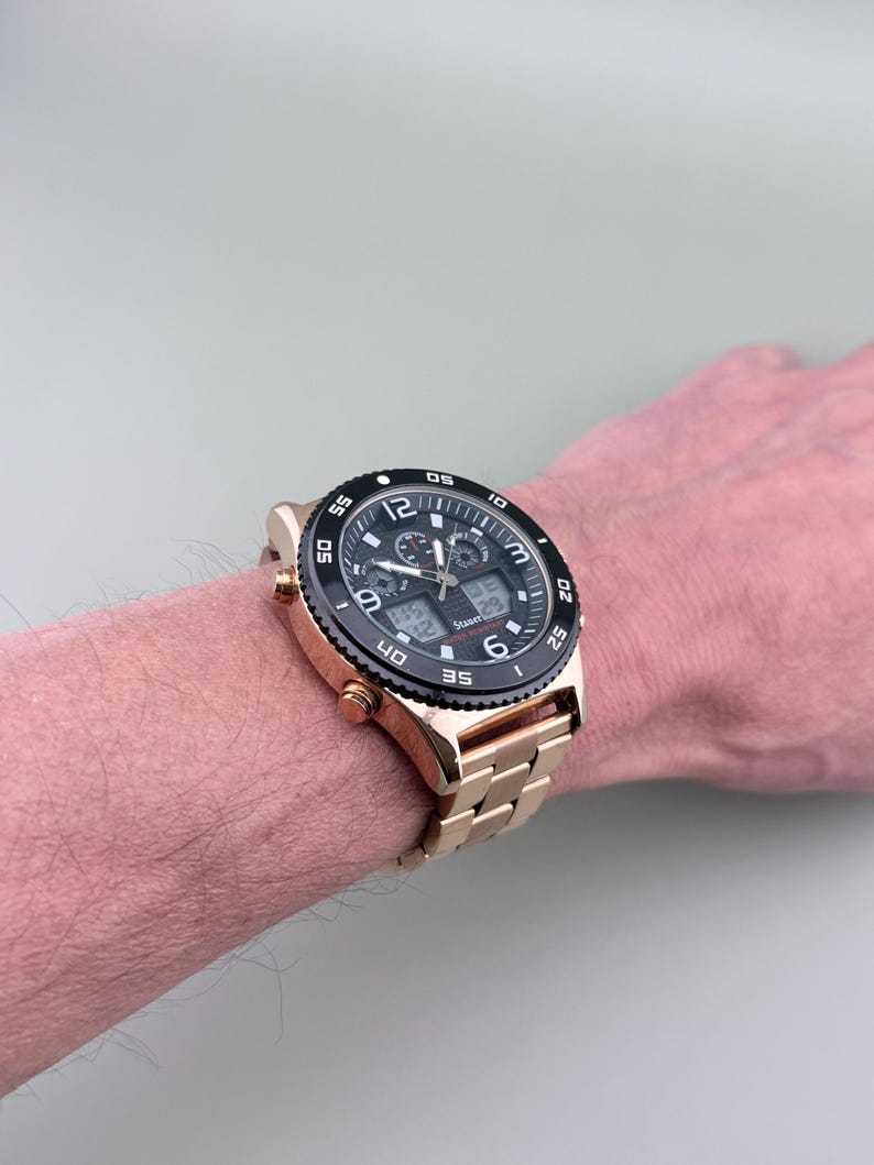 K&ouml;nnte beinhalten: Eine goldfarbene Armbanduhr mit schwarzer L&uuml;nette und schwarzem Zifferblatt. Die Uhr verf&uuml;gt &uuml;ber digitale Anzeigen und ein goldfarbenes Metallarmband. Die Uhr wird am Handgelenk getragen.