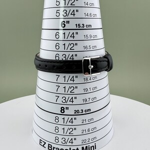 May include: A black leather bracelet with a silver buckle is shown on a white EZ Bracelet Mini sizing cone. The cone displays measurements in inches and centimeters, with the bracelet fitting at the 6-inch (15.3 cm) mark.