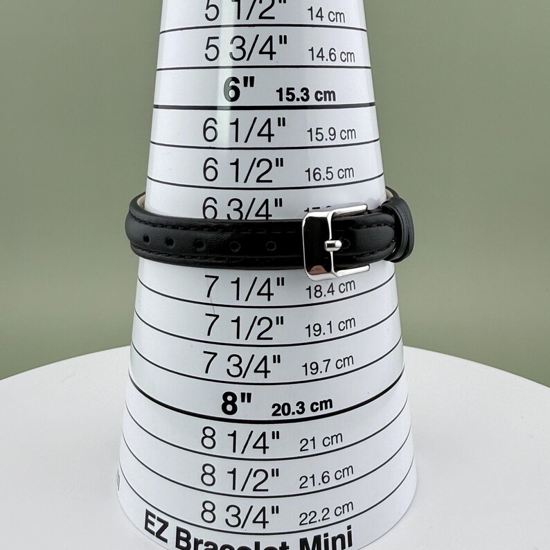 May include: A black leather bracelet with a silver buckle is shown on a white EZ Bracelet Mini sizing cone. The cone displays measurements in inches and centimeters, with the bracelet fitting at the 6-inch (15.3 cm) mark.