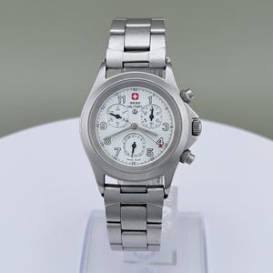Puede incluir: Un reloj Swiss Military de acero inoxidable con esfera blanca. El reloj cuenta con un cron&oacute;grafo con m&uacute;ltiples subesferas, una pantalla de fecha y agujas luminosas. La correa y la caja son de acero inoxidable.