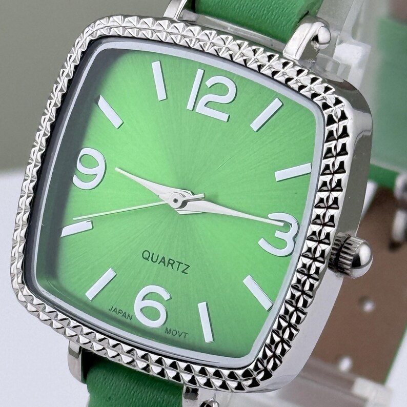 May include: A square-faced wristwatch with a bright green dial and a silver bezel. The watch has white numerals at the 12, 3, 6, and 9 o'clock positions. The watch strap is green. The word "QUARTZ" is printed on the watch face.