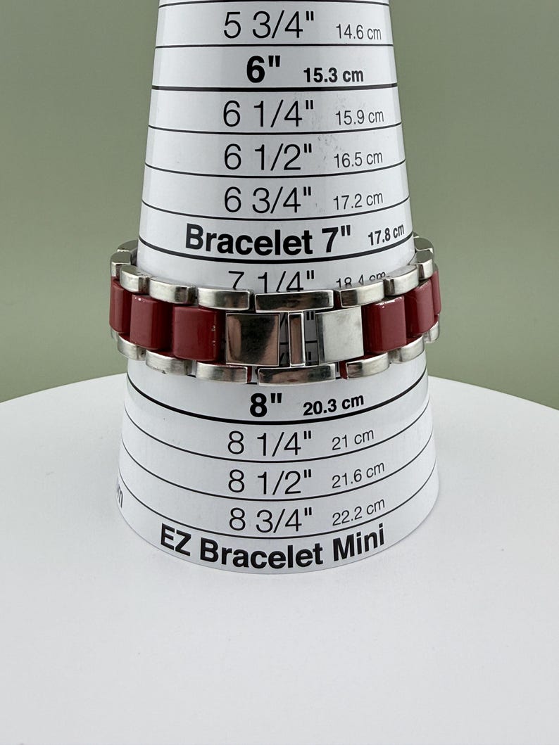 May include: A red and silver bracelet is displayed on a white and black EZ Bracelet Mini sizing tool. The bracelet is approximately 7 inches (17.8 cm) in length. The bracelet has a rectangular link design.
