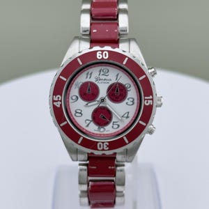 May include: A Geneva Platinum wristwatch with a silver-tone case and a red bezel and band. The watch face is white with red sub-dials and black numerals. The watch has a chronograph design.