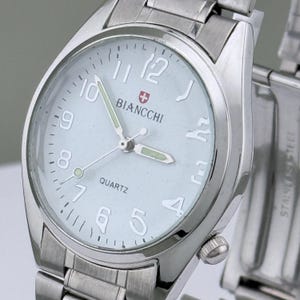 Pu&ograve; includere: Un orologio da polso argentato con quadrante azzurro chiaro. L'orologio presenta il marchio "BIANCCHI" e la scritta "QUARTZ". Ha un cinturino argentato e un quadrante rotondo con grandi numeri bianchi.