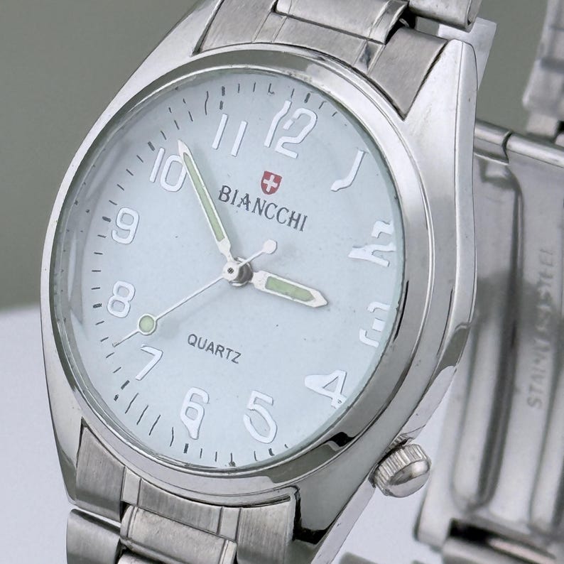 Pu&ograve; includere: Un orologio da polso argentato con quadrante azzurro chiaro. L'orologio presenta il marchio "BIANCCHI" e la scritta "QUARTZ". Ha un cinturino argentato e un quadrante rotondo con grandi numeri bianchi.