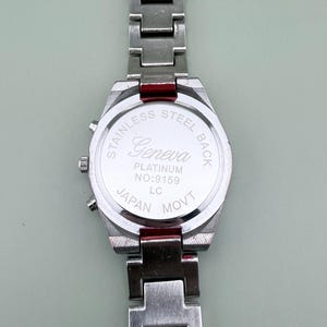 May include: A stainless steel Geneva watch with a silver band. The watch back is visible, displaying "Stainless Steel Back," "Geneva Platinum," and "Japan Movt." The watch has a rectangular face and a silver band.