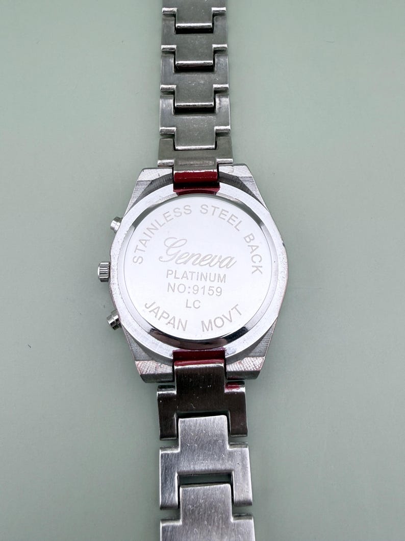 May include: A stainless steel Geneva watch with a silver band. The watch back is visible, displaying "Stainless Steel Back," "Geneva Platinum," and "Japan Movt." The watch has a rectangular face and a silver band.