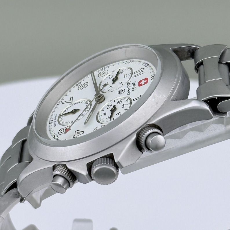 Puede incluir: Un reloj cron&oacute;grafo Swiss Military plateado con esfera blanca. El reloj presenta m&uacute;ltiples subesferas, visualizaci&oacute;n de fecha y correa de acero inoxidable. Dise&ntilde;o cl&aacute;sico y funcional.