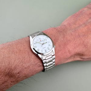 Pu&ograve; includere: Un orologio da polso argentato con quadrante bianco e numeri neri &egrave; mostrato. L'orologio ha un cinturino in metallo e il marchio "BIANCHI" &egrave; visibile sul quadrante. L'orologio &egrave; indossato al polso.