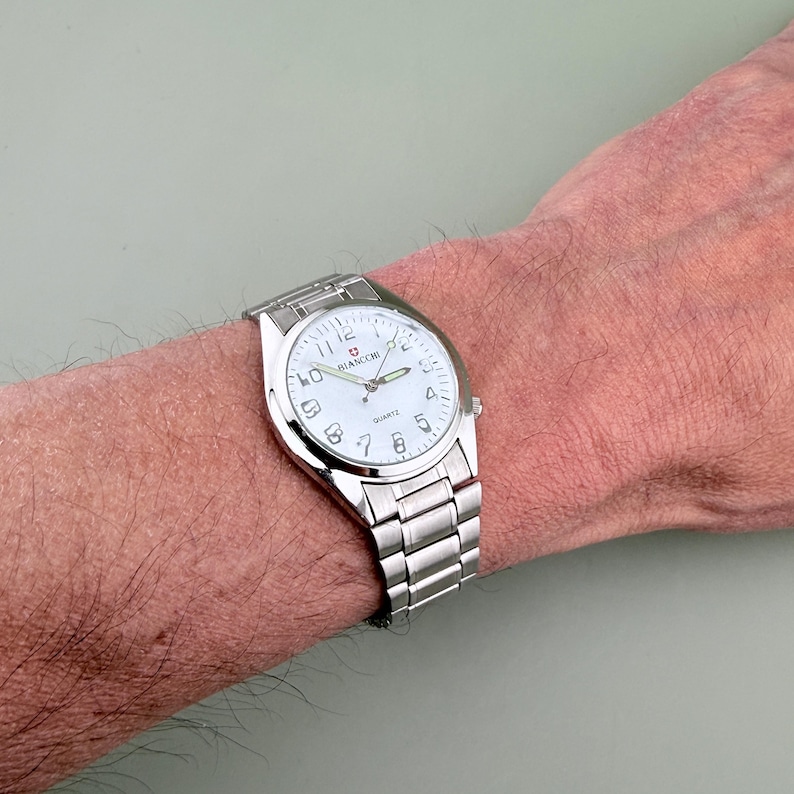 Pu&ograve; includere: Un orologio da polso argentato con quadrante bianco e numeri neri &egrave; mostrato. L'orologio ha un cinturino in metallo e il marchio "BIANCHI" &egrave; visibile sul quadrante. L'orologio &egrave; indossato al polso.