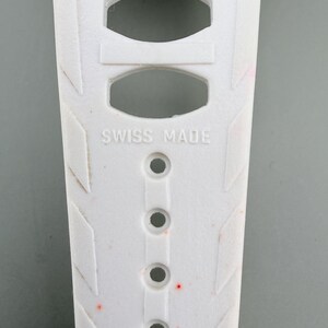 Puede incluir: Primer plano de una correa de reloj blanca con el texto "SWISS MADE". La correa tiene varios agujeros y patrones geom&eacute;tricos. La correa mide 16 mm de ancho.