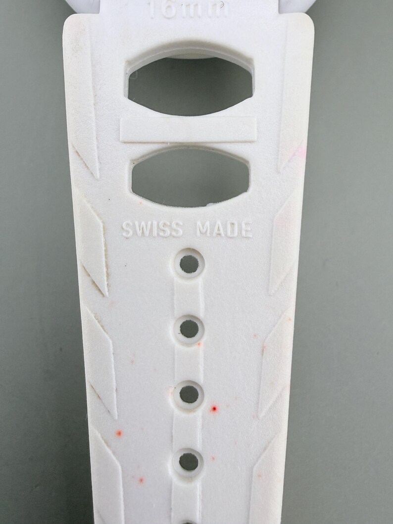 Puede incluir: Primer plano de una correa de reloj blanca con el texto "SWISS MADE". La correa tiene varios agujeros y patrones geom&eacute;tricos. La correa mide 16 mm de ancho.