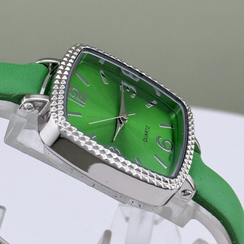 May include: A green quartz watch with a silver bezel and a green leather strap. The watch face is a vibrant green with silver hands and numerals. The watch has a rectangular face with rounded edges.