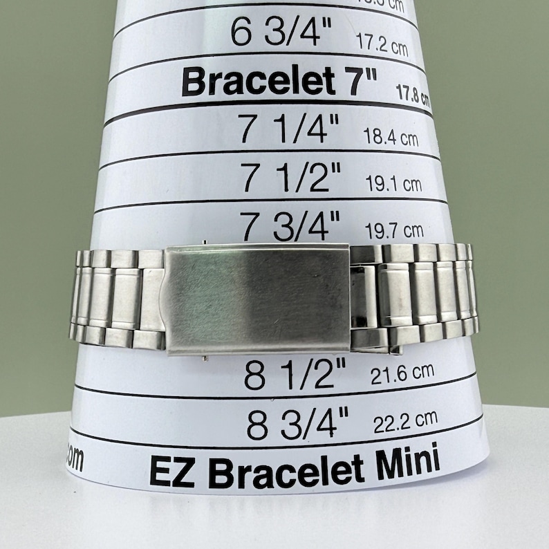 Pu&ograve; includere: Un braccialetto in metallo argentato &egrave; esposto su uno strumento di misurazione bianco EZ Bracelet Mini. Lo strumento presenta misure in pollici e centimetri, tra cui 7" (17,8 cm), 7 1/4" (18,4 cm) e 7 1/2" (19,1 cm).