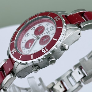 May include: A silver-toned wristwatch with a red bezel and accents. The watch face is white with red sub-dials and hands. The watch band is a combination of silver and red links. The watch has a chronograph function.