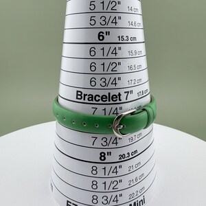 May include: A green bracelet with a silver buckle is displayed on a bracelet sizing cone. The cone shows measurements in inches and centimetres, with the bracelet fitting at the 17.8 cm mark.
