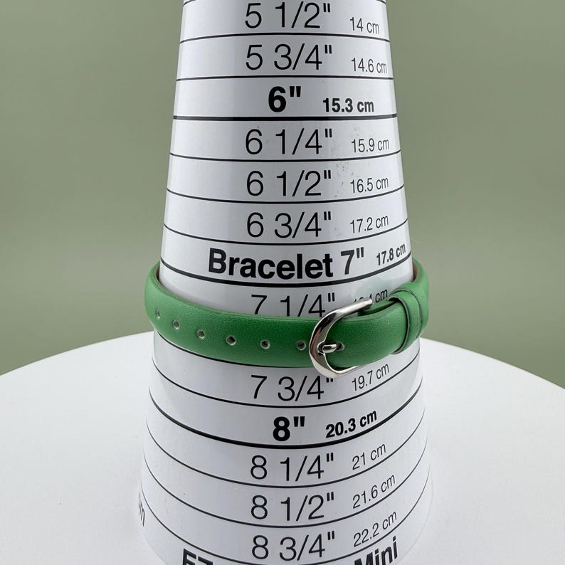 May include: A green bracelet with a silver buckle is displayed on a bracelet sizing cone. The cone shows measurements in inches and centimetres, with the bracelet fitting at the 17.8 cm mark.