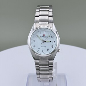Pu&ograve; includere: Un orologio da polso argentato con quadrante bianco e cinturino in metallo abbinato. Il quadrante mostra il marchio "Biancchi" e la parola "Quartz". L'orologio ha un quadrante rotondo con numeri e lancette nere.