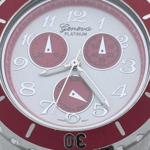 May include: A Geneva Platinum wristwatch with a silver face and red accents. The watch features three sub-dials, silver hands, and a red bezel. The numbers are white, and the watch has a stainless steel band.