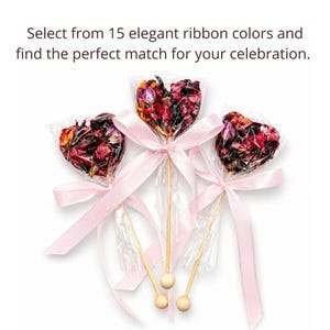 May include: Three heart-shaped favors filled with dried flower petals, wrapped in clear cellophane, and tied with pink satin ribbons. The favors are on wooden sticks with a small wooden ball at the end. Text reads: Select from 15 elegant ribbon colors and find the perfect match for your celebration.