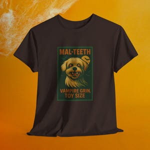 May include: A dark brown t-shirt featuring a Halloween-themed graphic. The graphic includes a cartoon dog with vampire teeth, the text "MAL-TEETH", and "VAMPIRE GRIN, TOY SIZE". The design is set against a green background.