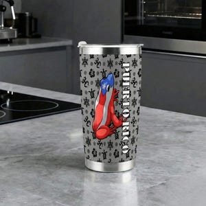 May include: A stainless steel travel tumbler featuring a red, white, and blue frog design with the Puerto Rican flag. The tumbler has a gray background with a repeating pattern and the word "PUERTO RICO" printed vertically.