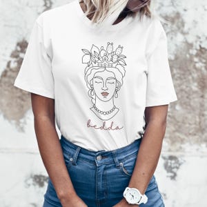 May include: White t-shirt featuring a line drawing of a woman's face wearing a crown of lemons and cactus. The text "bedda" is printed below the image.